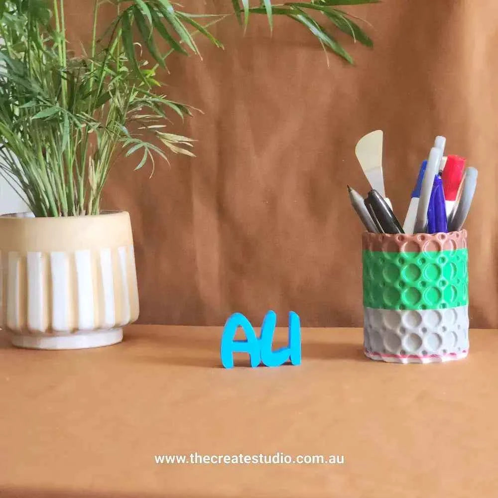 Custom name decor gift in blue beside a colorful pen holder and green plant for stylish home decor