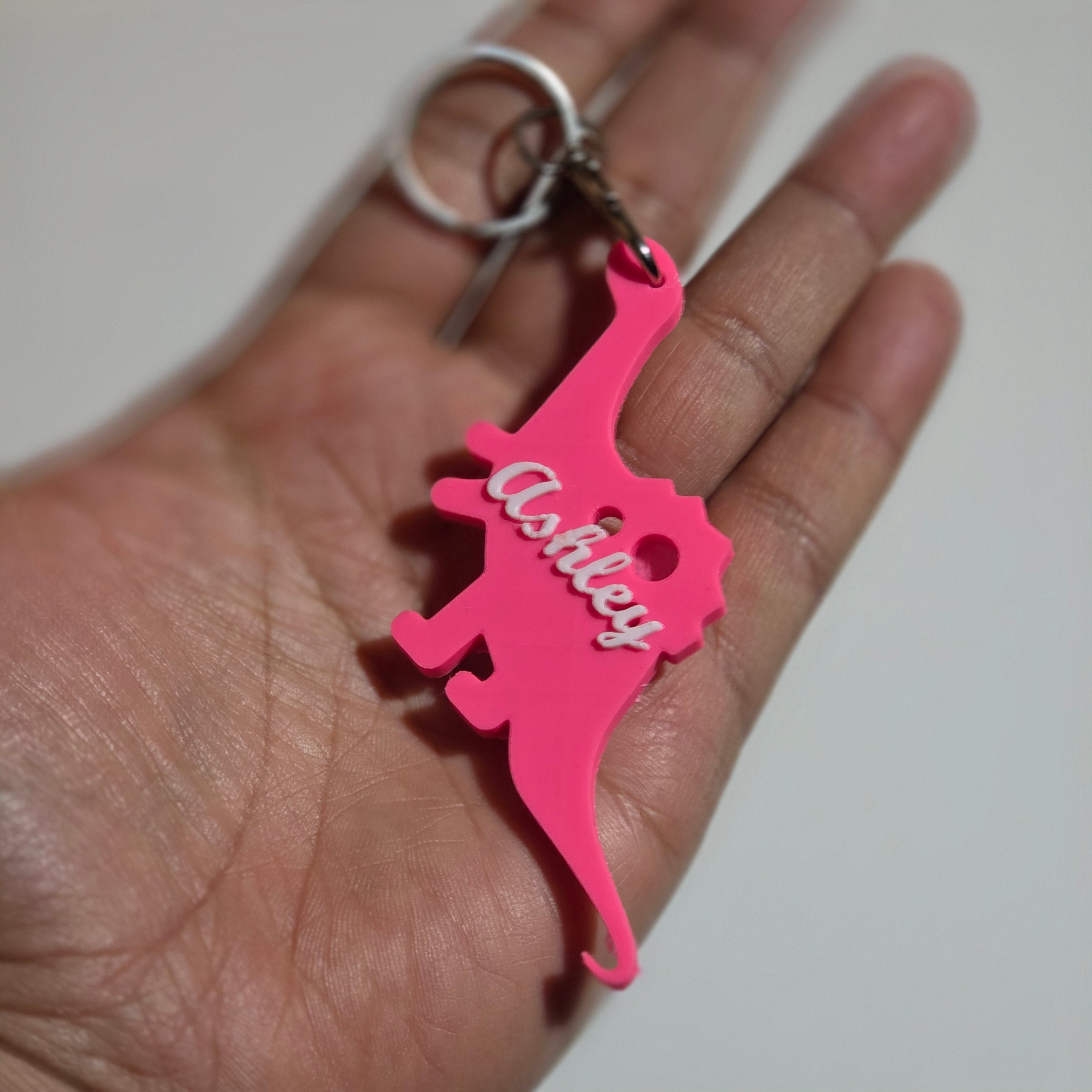 Custom name dino keychain in bright pink with the name Ashley attached to a metal keyring
