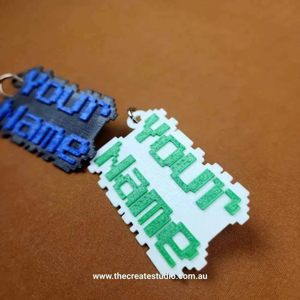 Custom pixelated name keychain in blue and green on a brown background by The Create Studio
