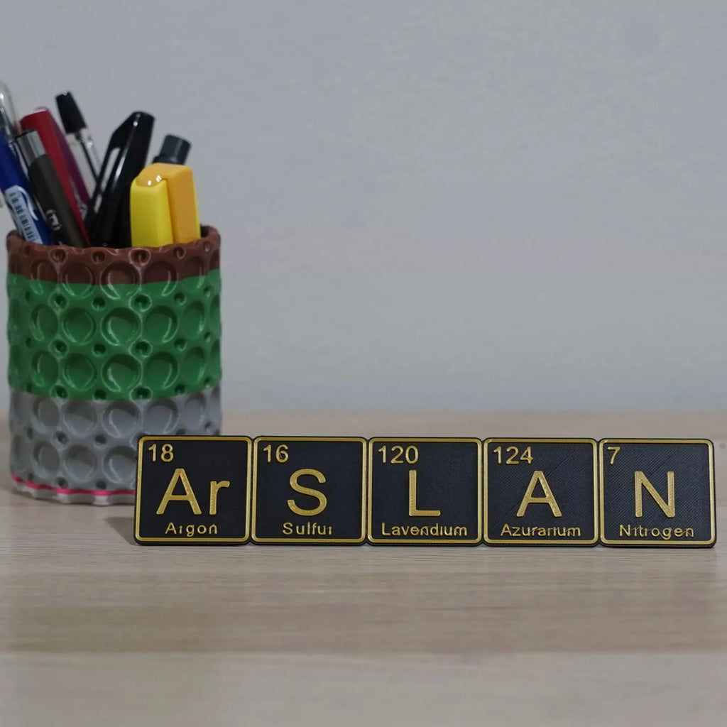 Personalized periodic table name plate spelling 'ARSLAN' with a colorful pen holder in the background.