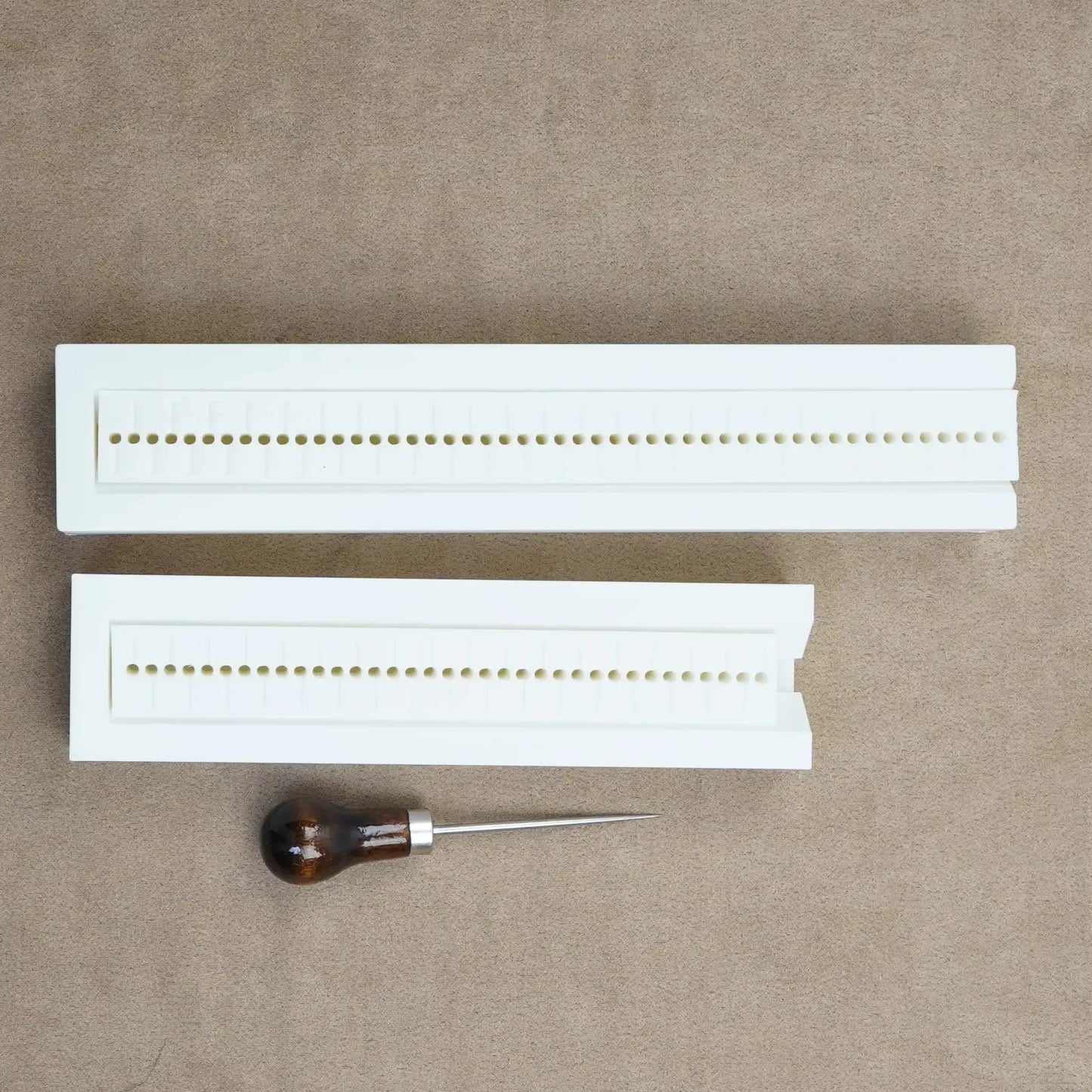 Hole punch guide for bookbinding, featuring two white guides and a wooden-handled awl for custom journaling.