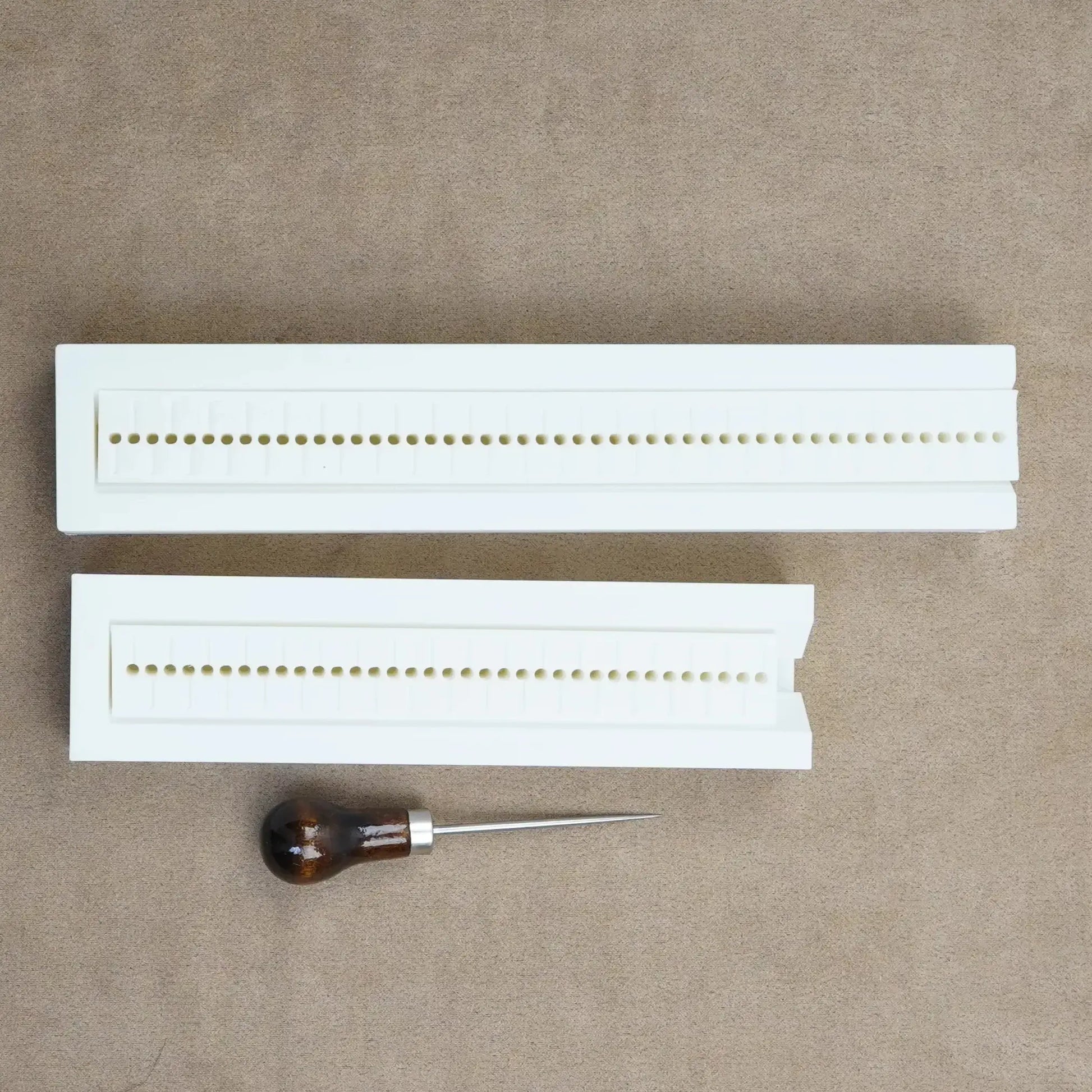 Hole punch guide for bookbinding, featuring two white guides and a wooden-handled awl for custom journaling.