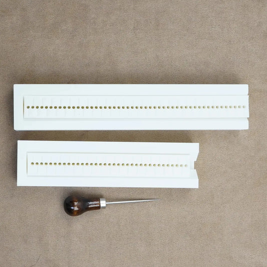 Hole punch guide for bookbinding, featuring two white guides and a wooden-handled awl for custom journaling.