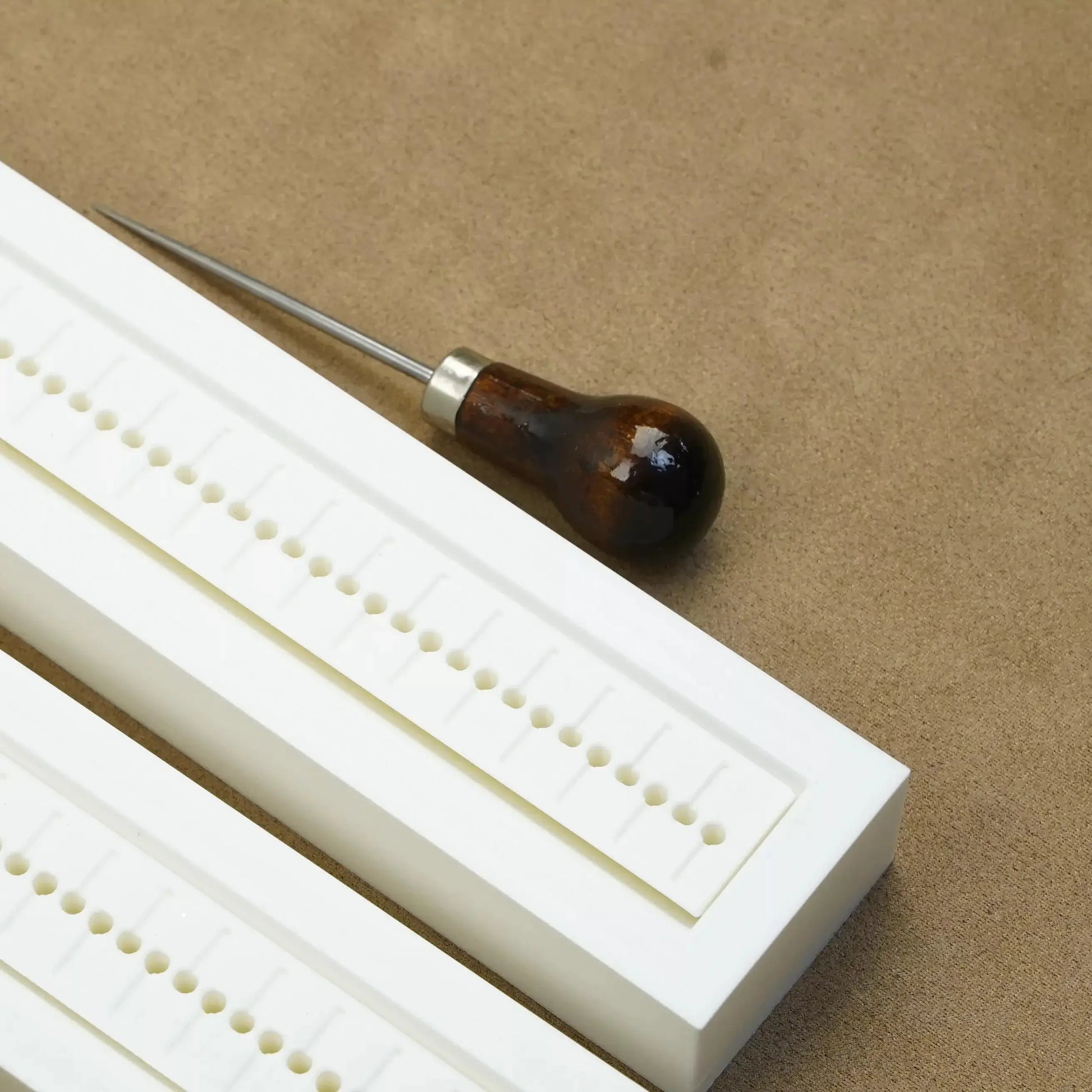 Hole punch guide and crafting tool on a beige surface, ideal for bookbinding and scrapbooking projects.