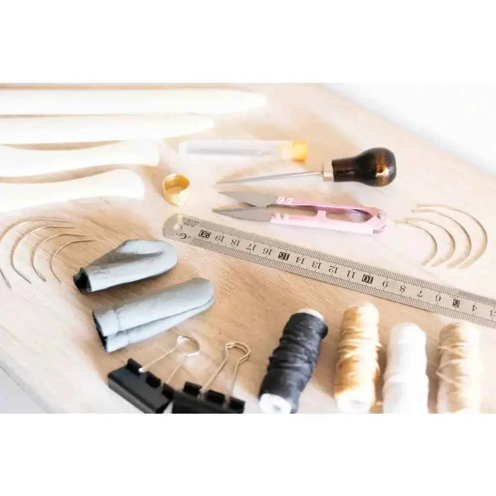 Book binding sewing set with tools including needles, threads, and a ruler on a wooden surface