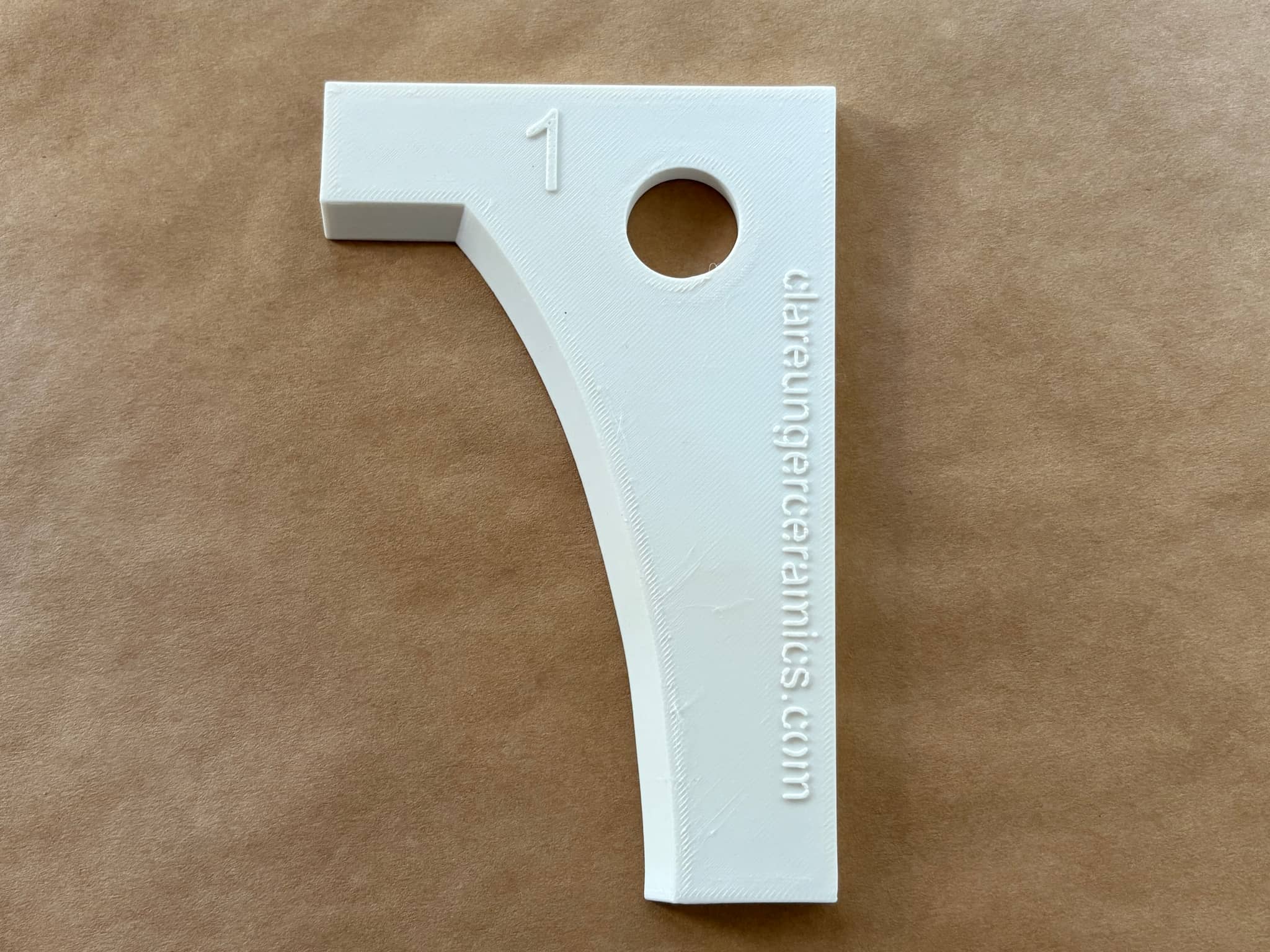 Ceramic item designed by Clare Unger with the number one and a hole for hanging or display