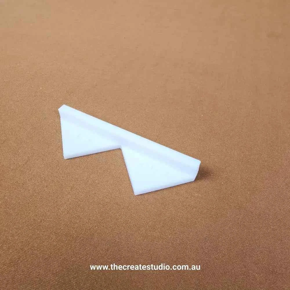 White plastic book binding corner pieces on brown fabric background showing triangular protective edge by The Create Studio
