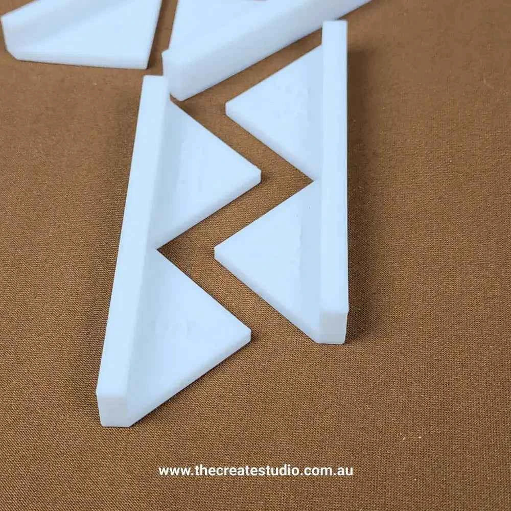 White plastic triangular book binding corner pieces on brown fabric background by The Create Studio