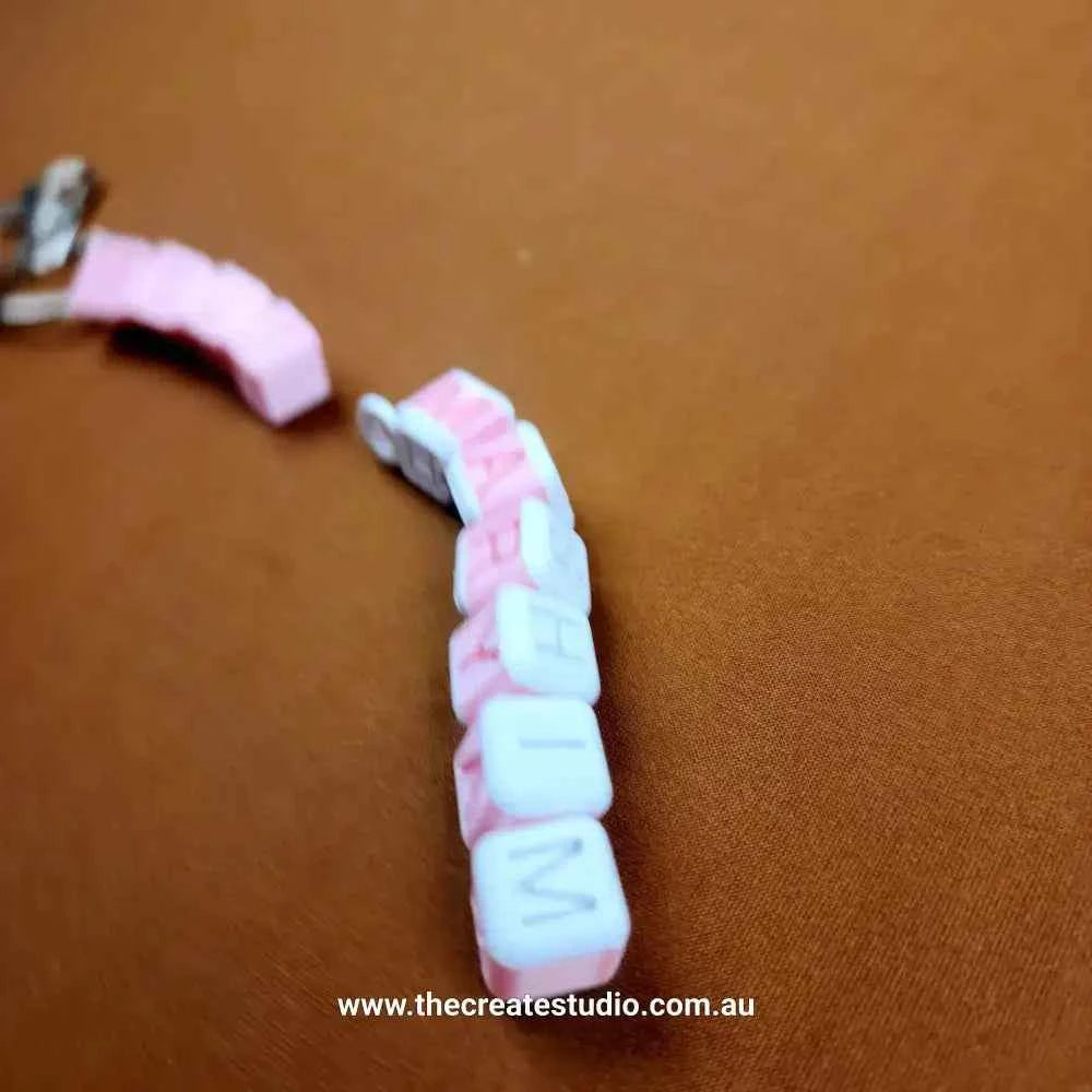 Personalised name keychain in pink and white beads spelling a name on a brown background
