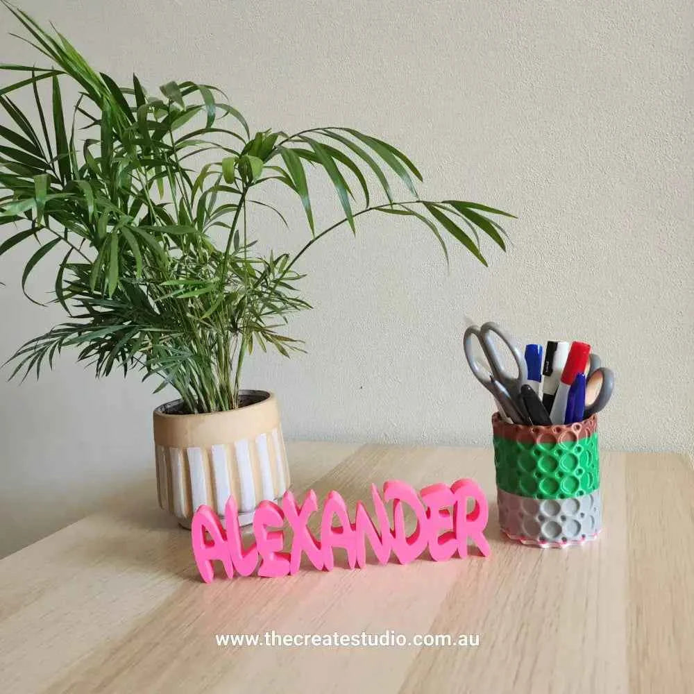 Custom name decor gift in pink spelling ALEXANDER on a wooden table with a plant and pen holder