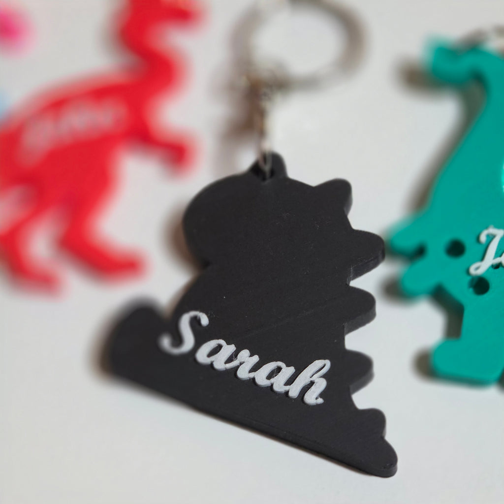 Custom name dino keychain in black with Sarah design alongside colorful dino shapes
