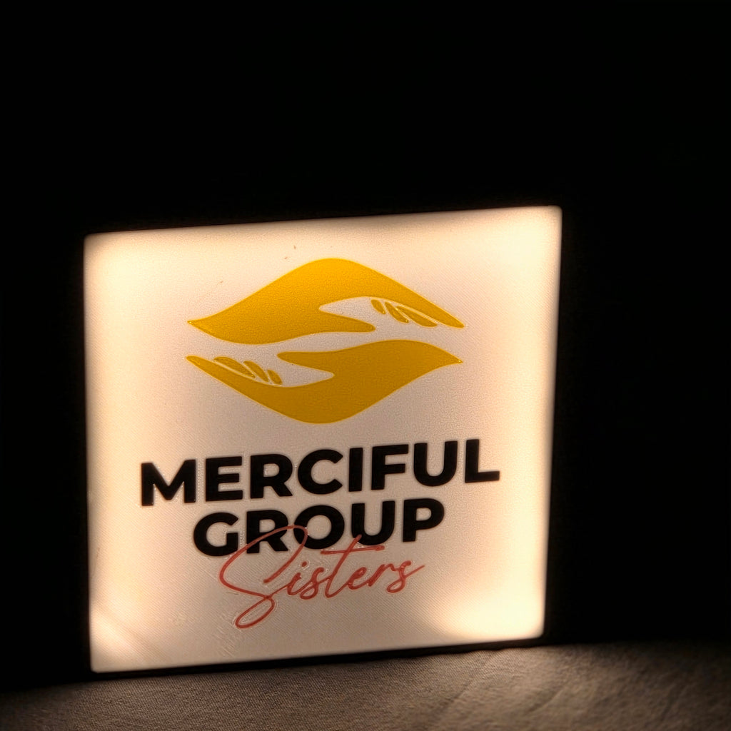 Illuminated square branded sign displaying Merciful Group Sisters logo on unique corporate desk light box