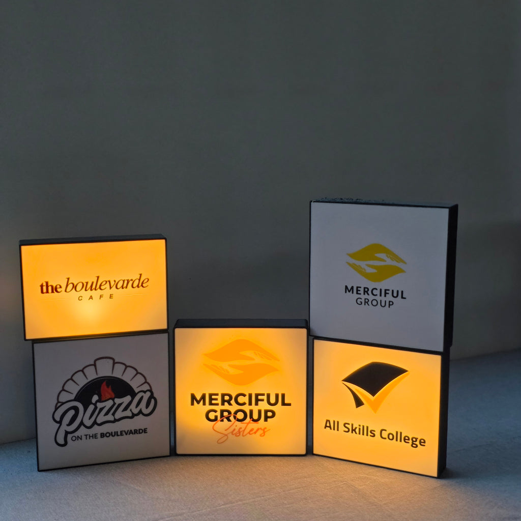 Stacked illuminated branded logo panels in warm amber light from a unique corporate desk light box by The Create Studio