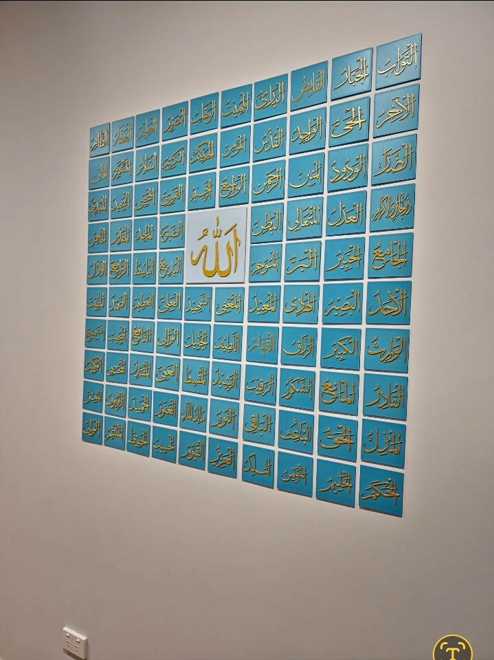 99 Names of Allah wall art in gold calligraphy on blue tiles displayed on a white wall
