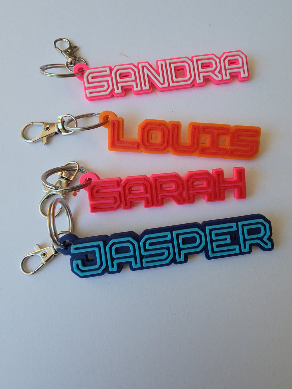 Personalised name keyring set featuring colourful designs for custom names like Sandra, Louis, Sarah, and Jasper
