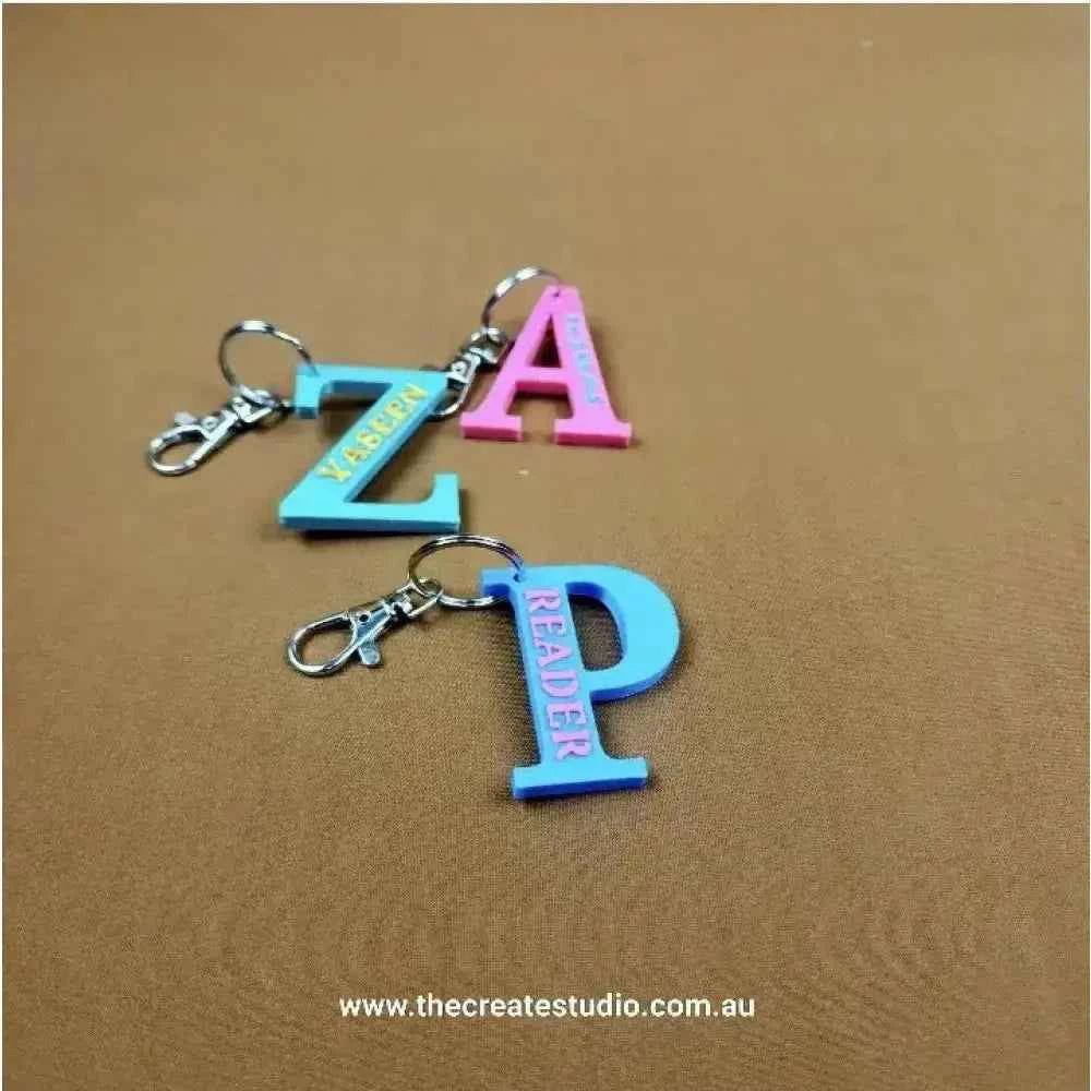 Two personalised initial keychains in pink and blue, featuring letters Z, A, P, and R