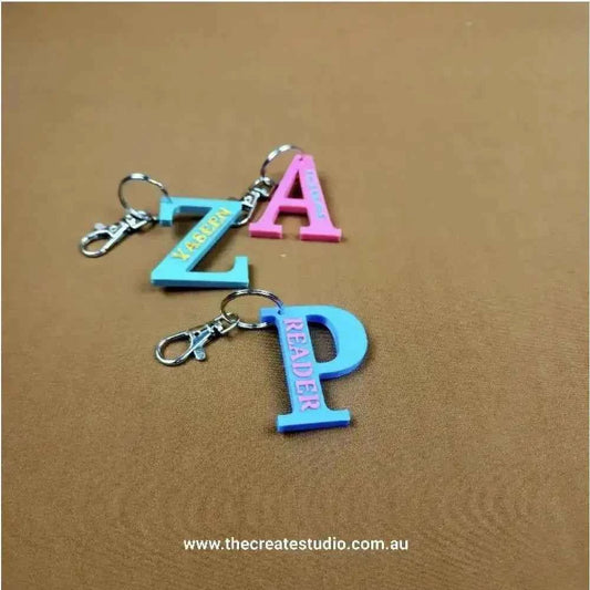 Two colorful personalized initial keychains in pink and blue with clips for easy attachment