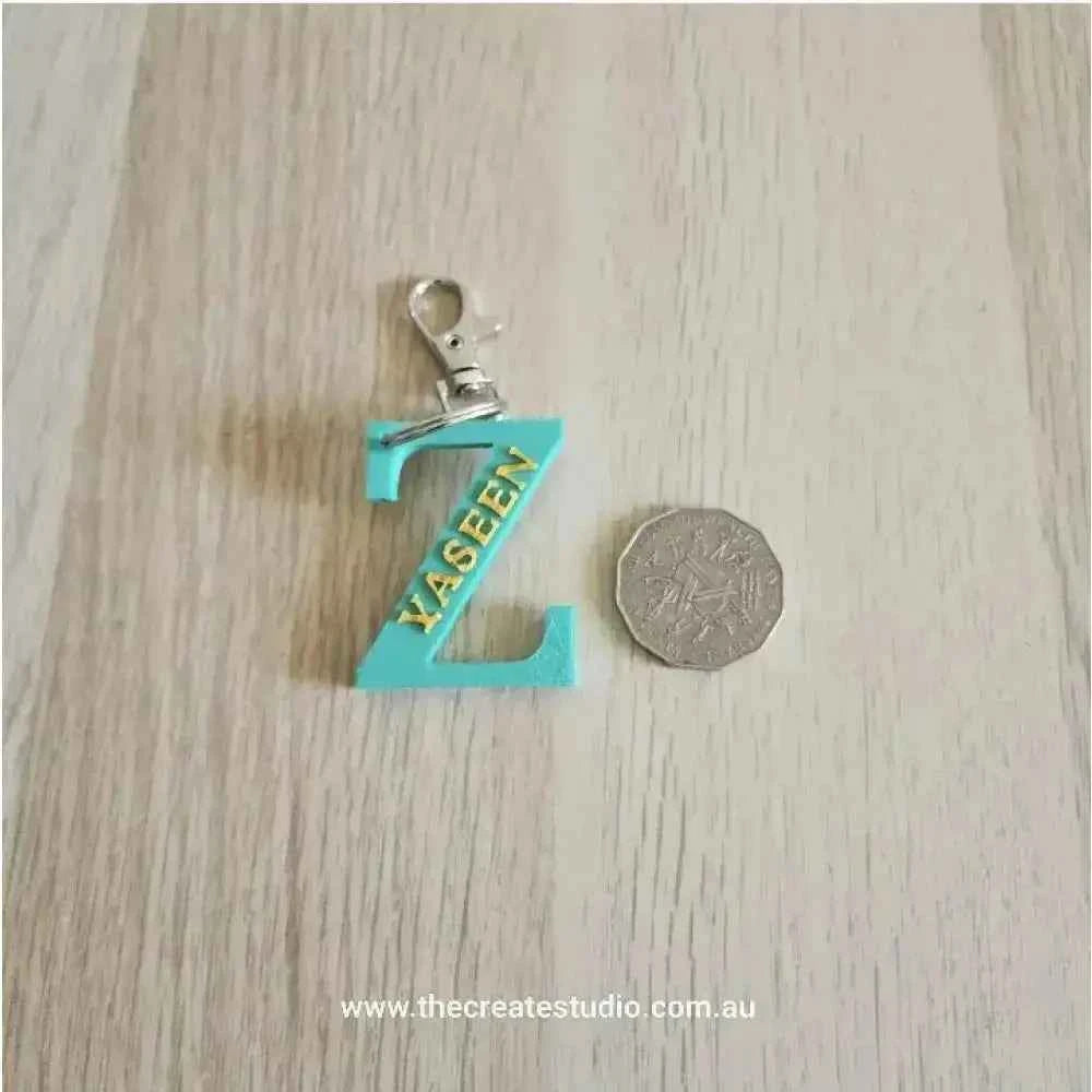 Personalized initial keychain with turquoise 'Z' design next to a coin for size reference