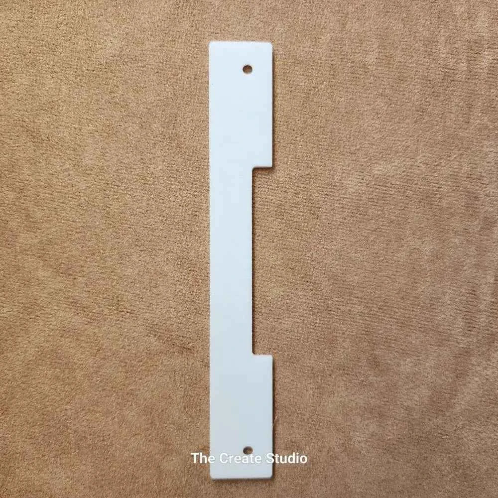 The Create Studio white plastic bee hive entrance reducer with slots and mounting holes on a brown fabric background