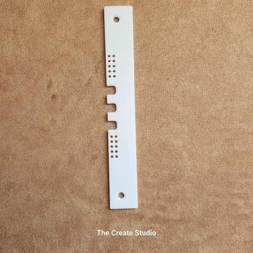 White plastic bee hive entrance reducer strip with three notches and ventilation holes on brown background