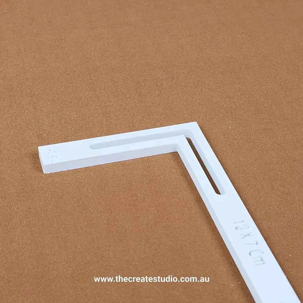 White L-piece bookbinding tool plastic corner guide with ruler markings on brown background