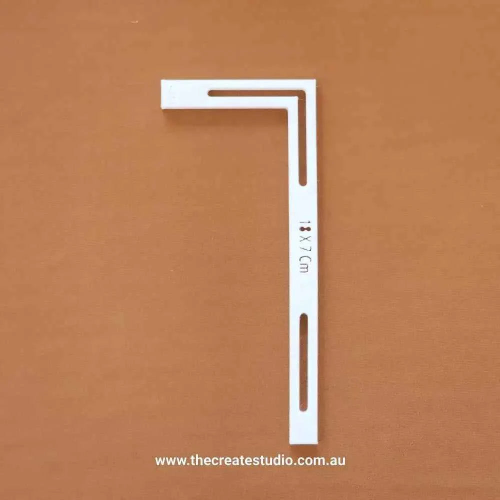 White L-piece bookbinding tool with measurement markings and elongated slots for precise corner alignment