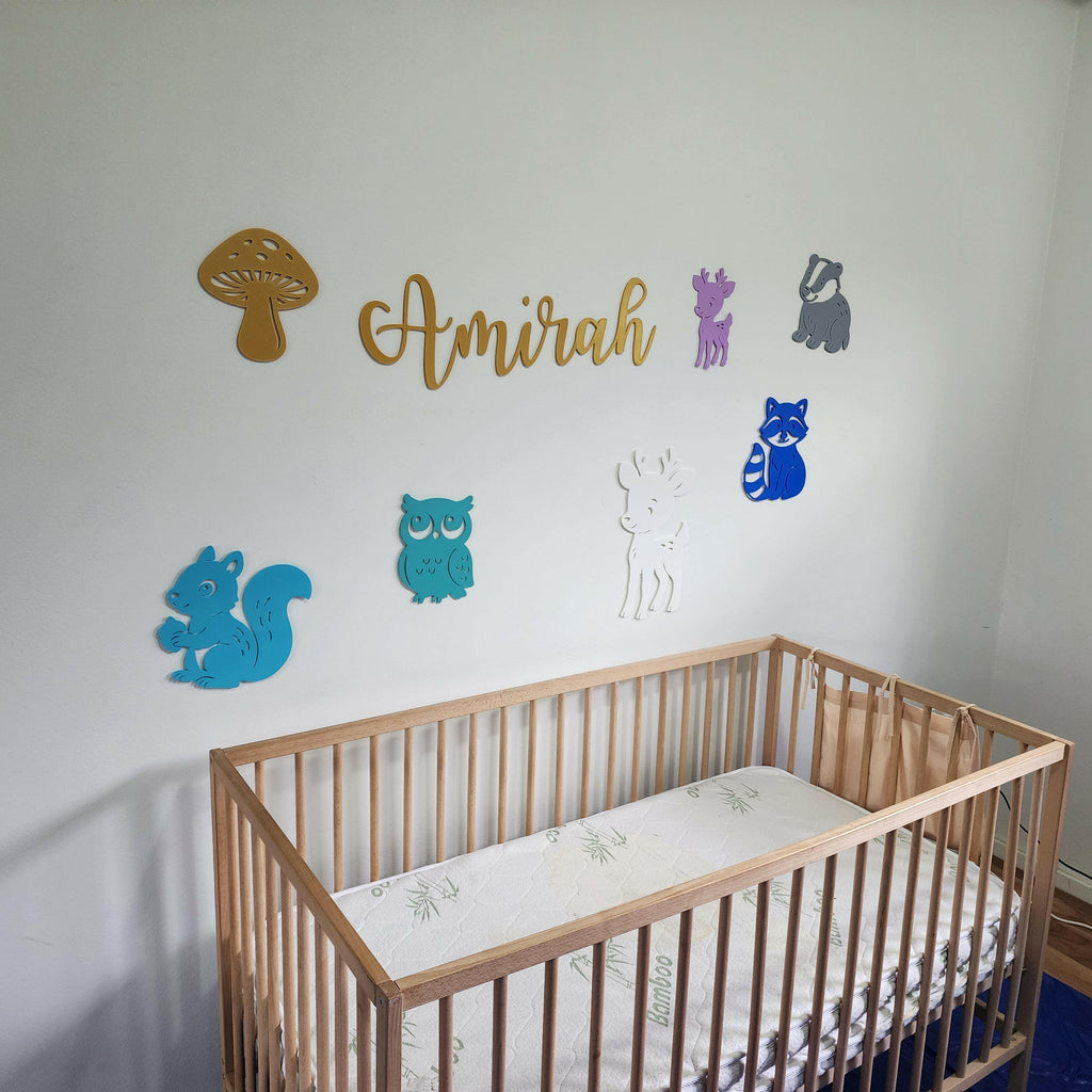 Woodland creature nursery decorations by The Create Studio above wooden baby crib with animal shapes and name Amirah