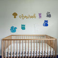 Wooden crib with colorful woodland creature nursery decorations including squirrel, owl, deer, raccoon, and badger on wall